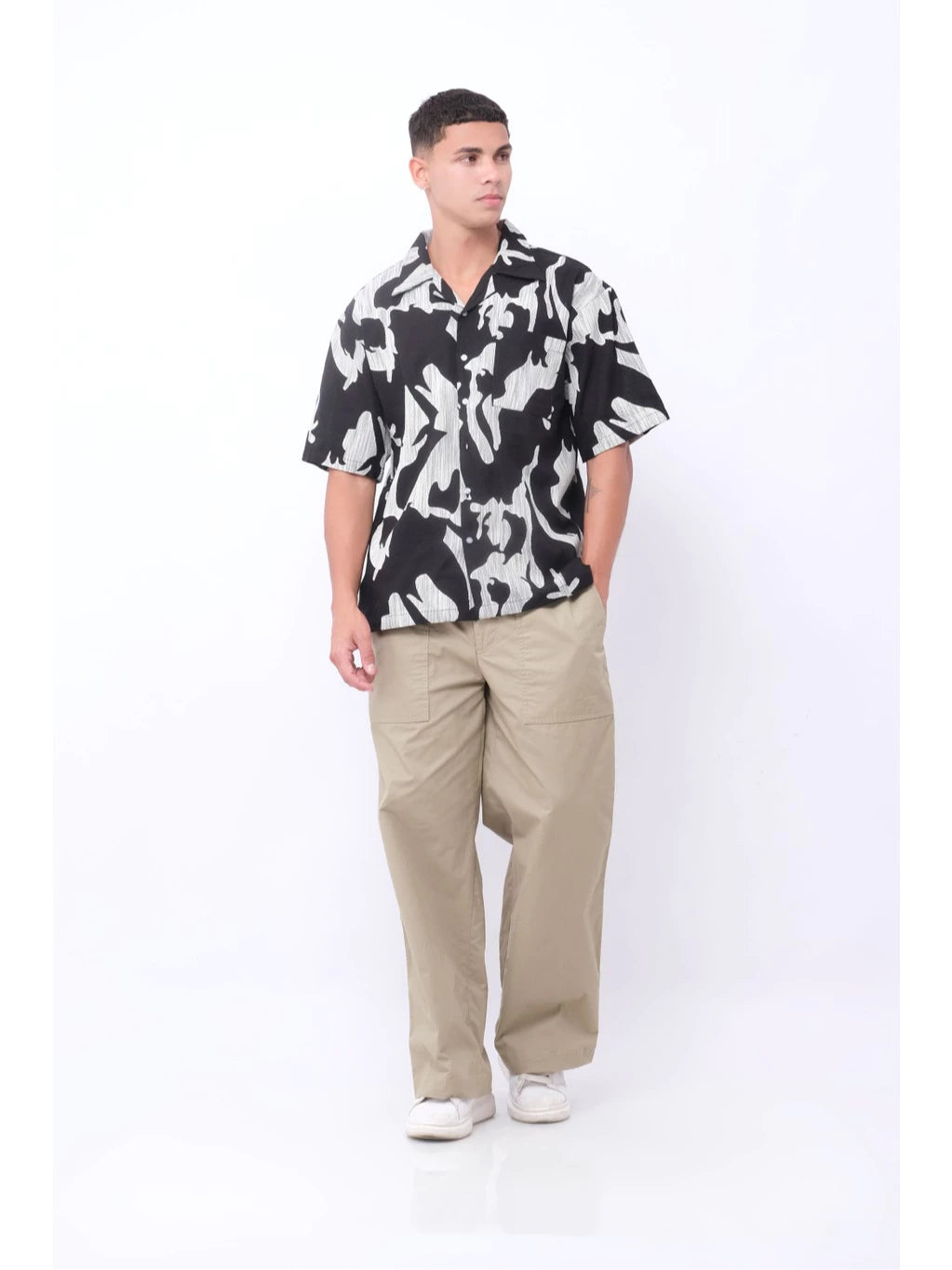 Man wearing a black and white patterned shirt by Blee with beige pants on a white background