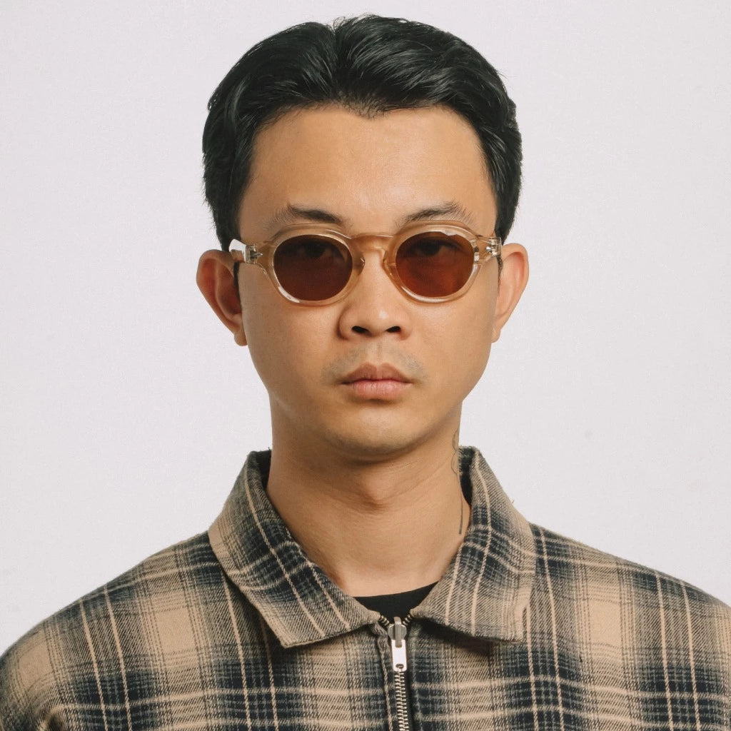 Man wearing round sunglasses by Cool Uncle and a plaid jacket against a plain background