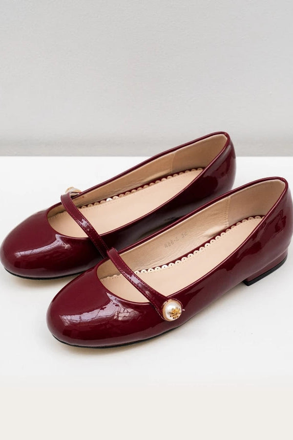 Pair of maroon patent leather flat shoes with a gold buckle on a white background