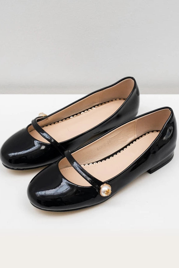 Pair of black patent leather flat shoes with a pearl detail on a white background