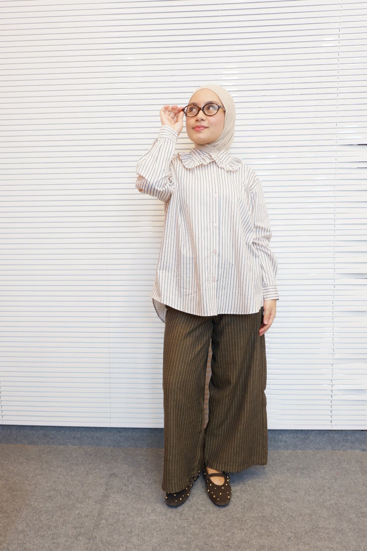 Person wearing a pink striped shirt by Tuff Puff and hijab standing on a checkered floor.