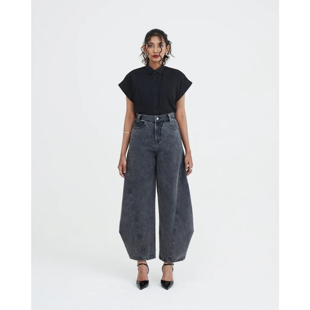 Person wearing a black top and wide-leg jeans by Achete de Nous on a white background