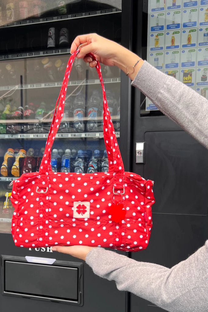 Red polka dot shoulder bag by Luella held in front of a vending machine.