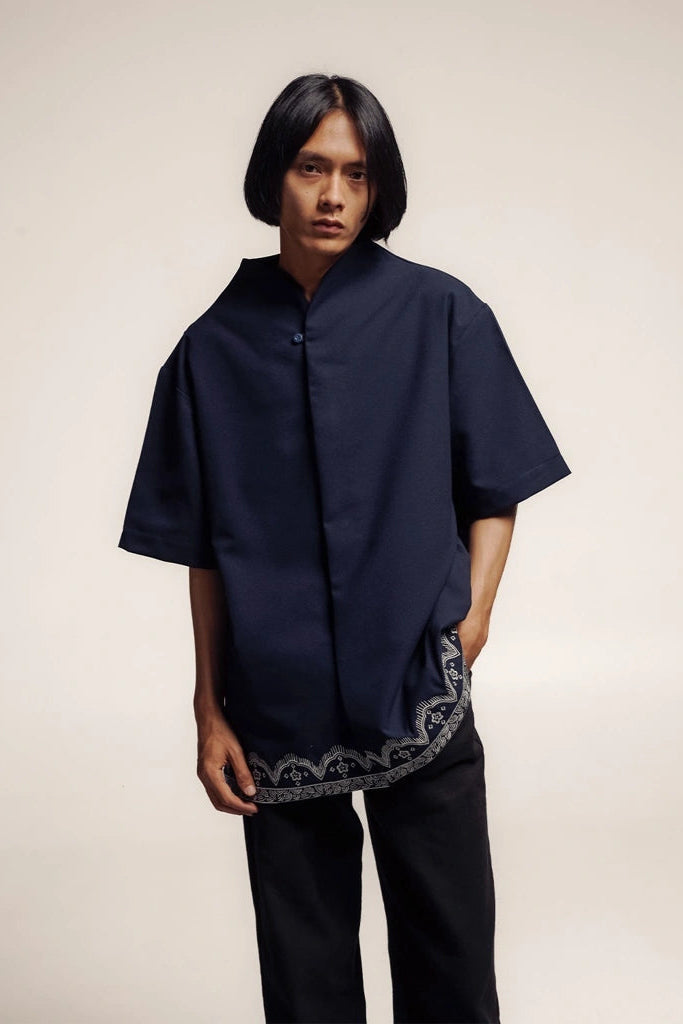 Person wearing a dark blue shirt with a embroidered hem by Damakara on a plain background