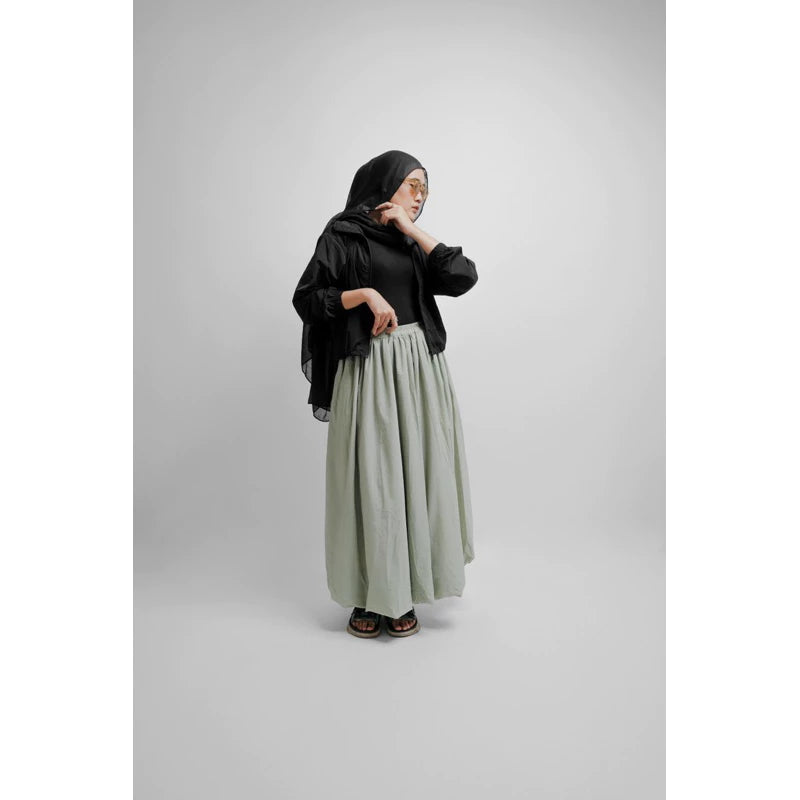 Woman wearing a flowy sage green maxi balloon skirt styled with a black top and outerwear.