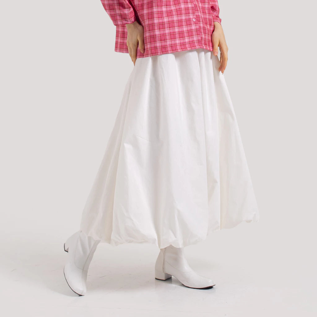 A person standing wearing a white balloon puff skirt with a full rubber waistband and a pair of white boots.