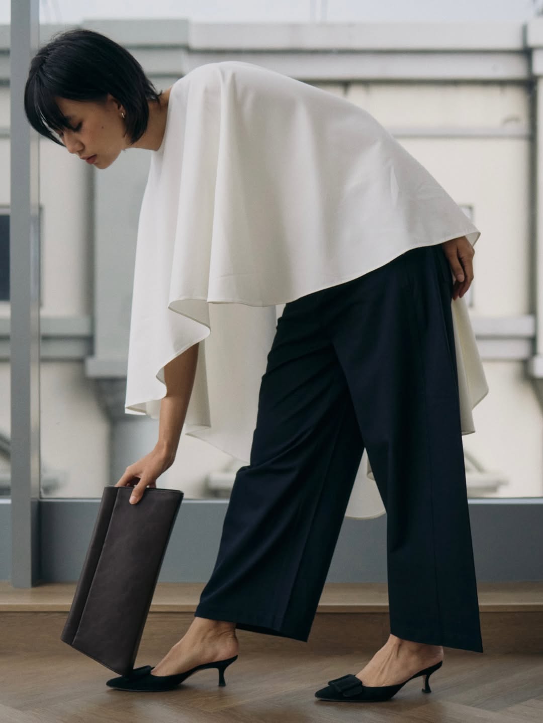 Person wearing a white top and navy pants holding a black women's clutch bag.
Seorang wanita mengenakan atasan putih dan celana navy, memegang tas clutch wanita berwarna hitam.