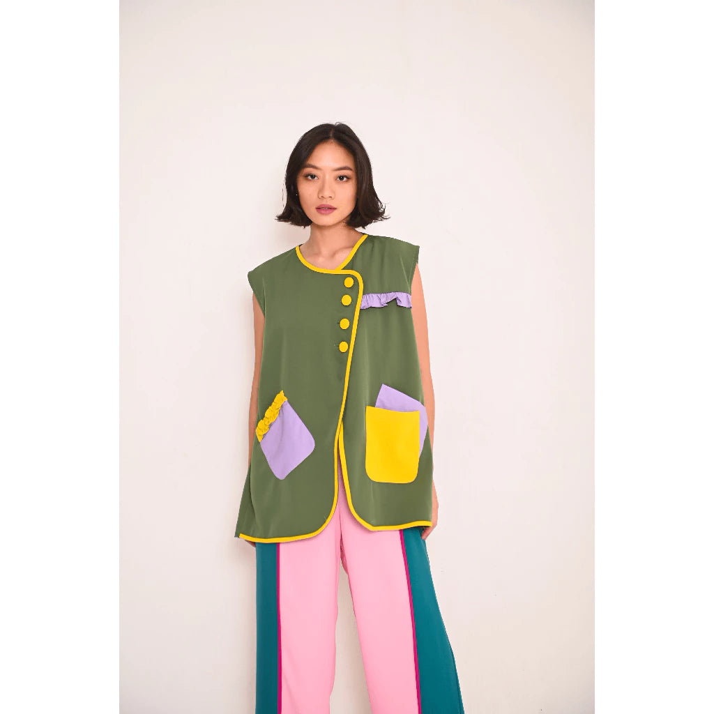 A model wearing Briona Vest, a green sleeveless vest with yellow and purple details from Senora The Label, paired with pink and blue trousers.