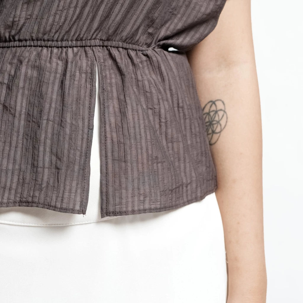 Close-up of a person wearing a textured brown top by Isoos Studios with a white background