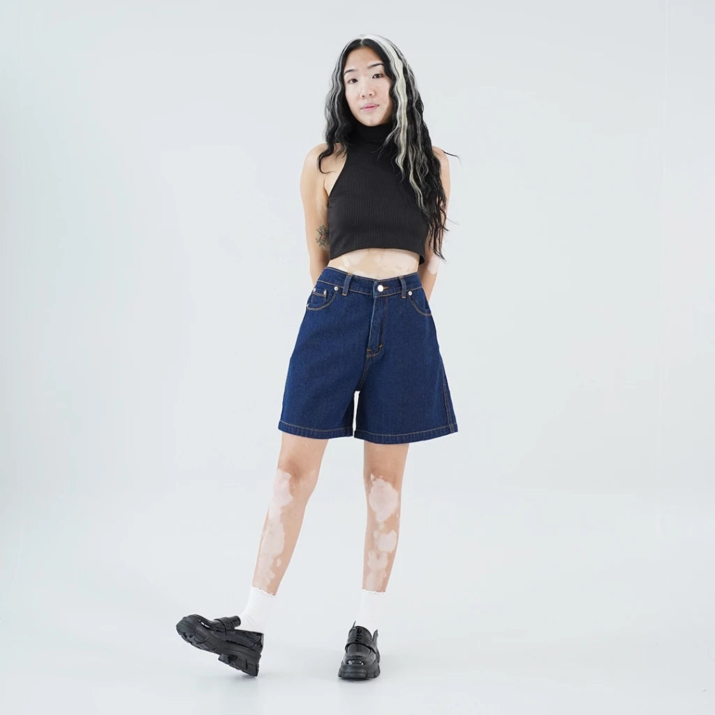 A person wearing a black halter top and dark blue jorts pants, with a pair of black flat shoes.