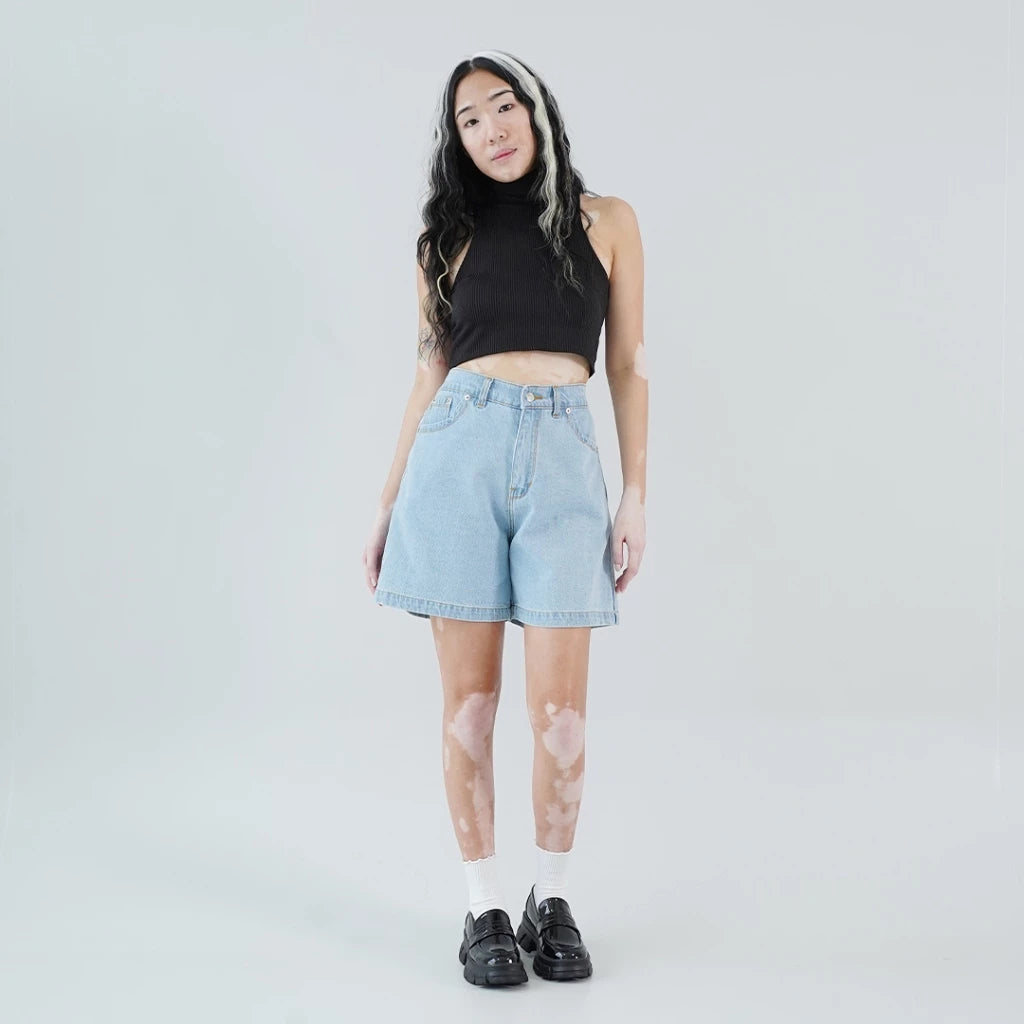 A person wearing a black halter top and light blue jorts pants, with a pair of black flat shoes.