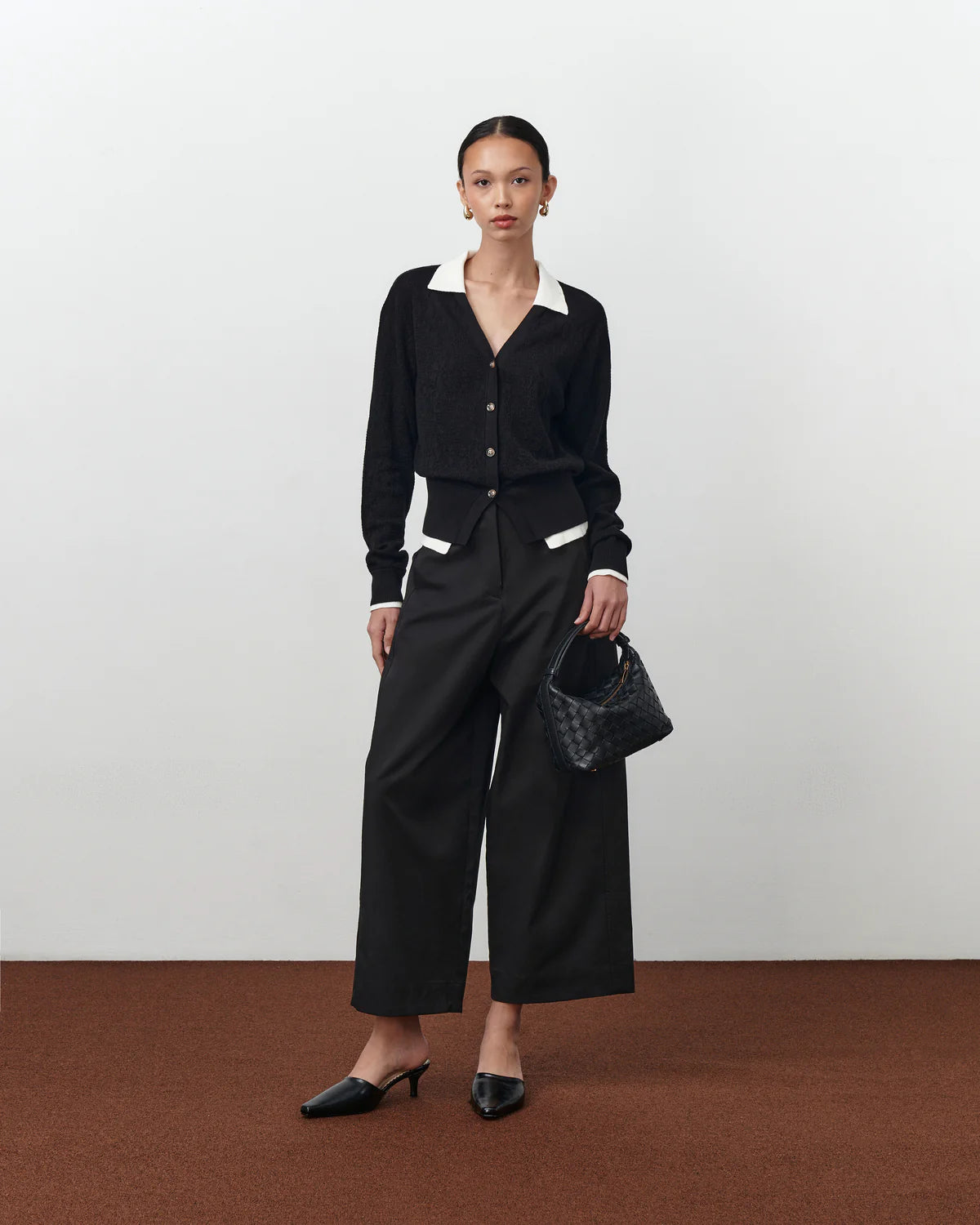 Woman wearing a black cardigan by Achete De Nous, holding a black handbag on a white background.