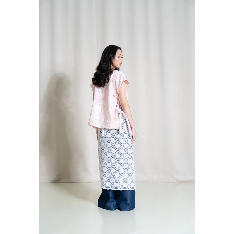 A person standing in a studio setting, wearing a white top and the Cemara Lace Skirt in white. The skirt is long and has a floral pattern.