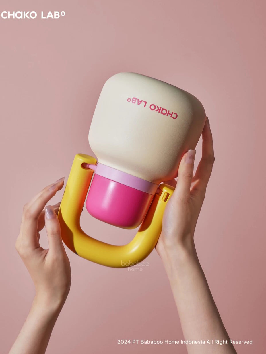 Colorful baby bottle from Chako Lab held by hands against a pink background