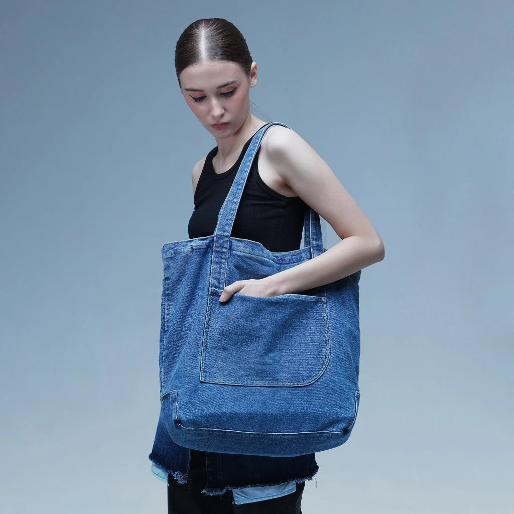 Woman wearing a large blue denim totebag against a gray background
Seorang wanita mengenakan tas jinjing denim biru besar di latar belakang abu-abu