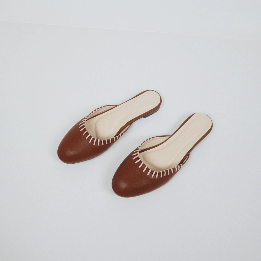 Pair of Amara Sol brown flatshoes with white trim on a light gray background