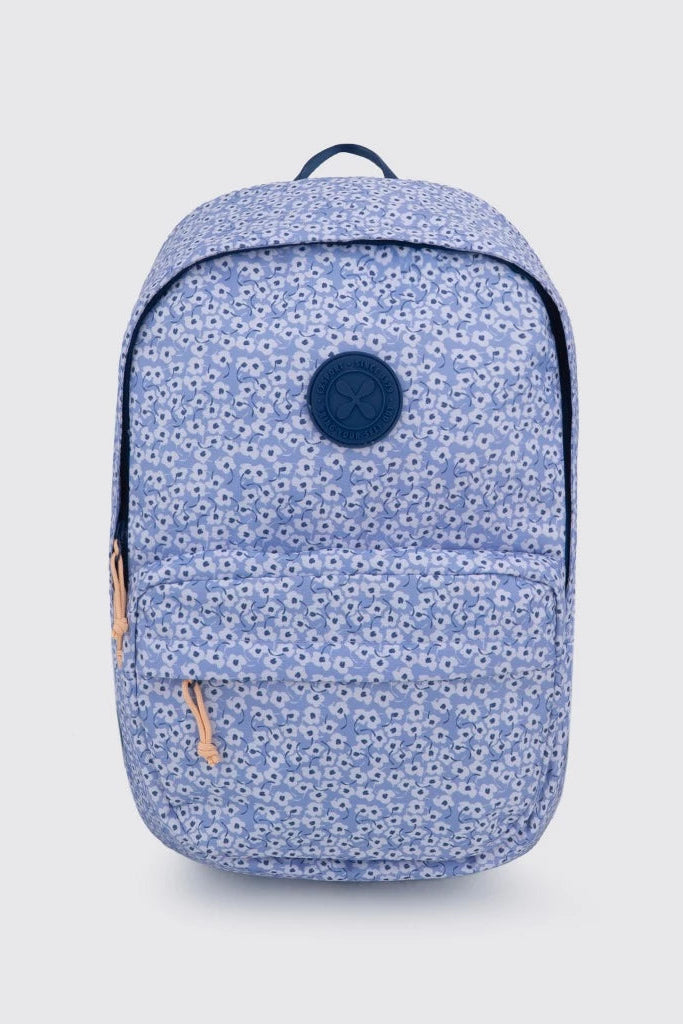 A light blue backpack by Exsport Bag with a dense white floral print, featuring a dark blue circular logo patch on the front pocket and a matching dark blue top handle, set against a light gray background.