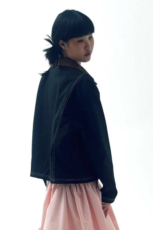 Person wearing a black work jacket and pink skirt on a white background
