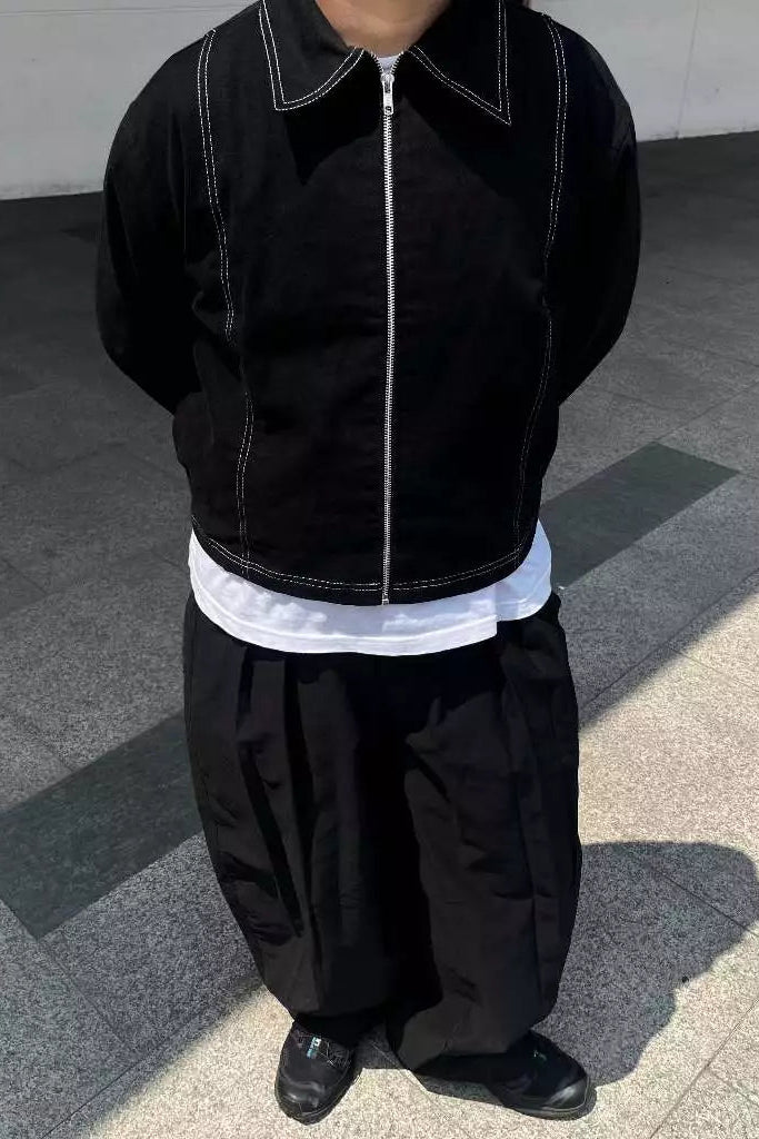 Person wearing a black work jacket and pants with a white shirt underneath, standing on a concrete surface.