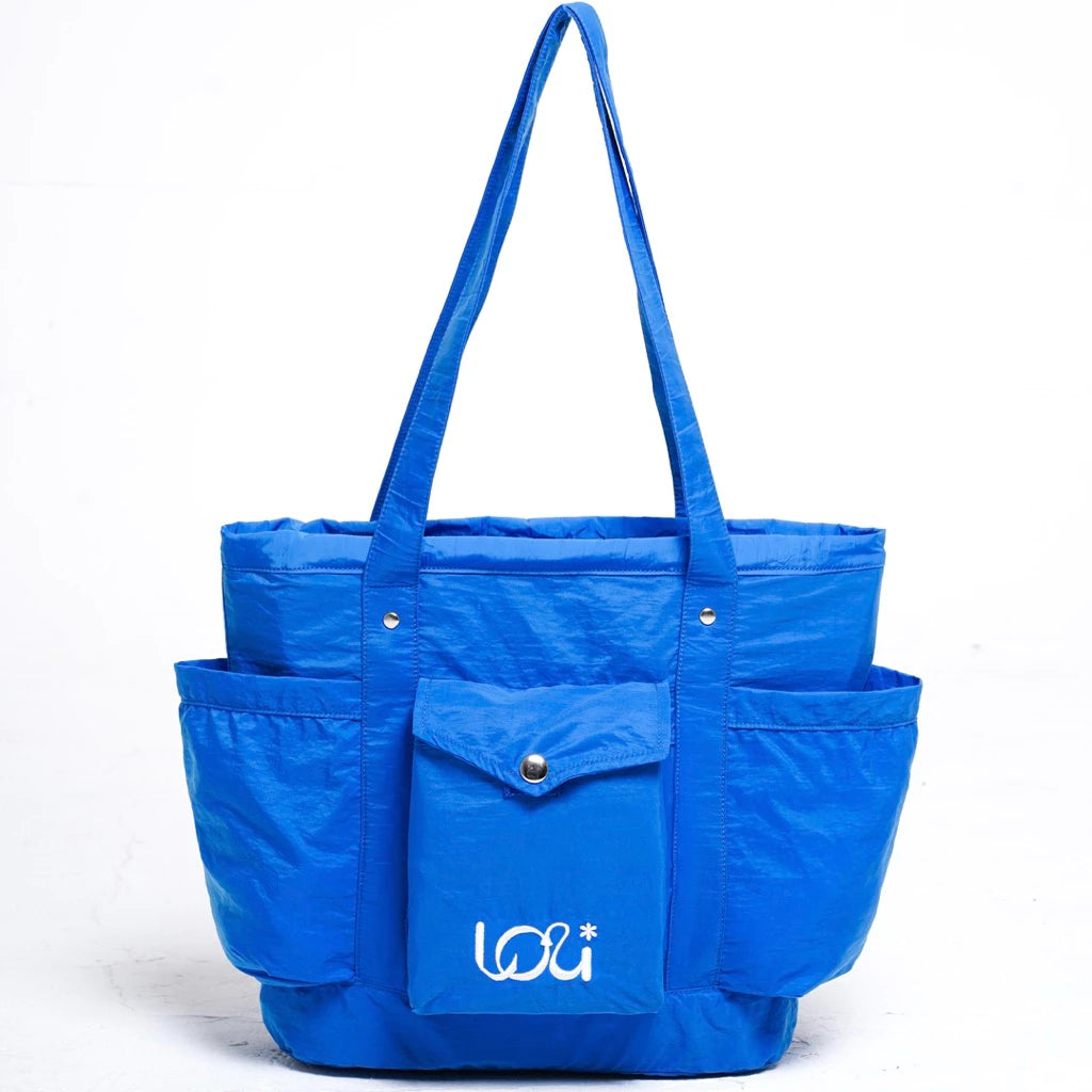 Blue women’s tote bag featuring two long handles, a front flap pocket with button closure, and two spacious side pockets.
Tas wanita warna biru dengan desain tote bag, dilengkapi dua handle panjang, satu kantong depan berpenutup kancing, serta dua kantong samping yang luas.