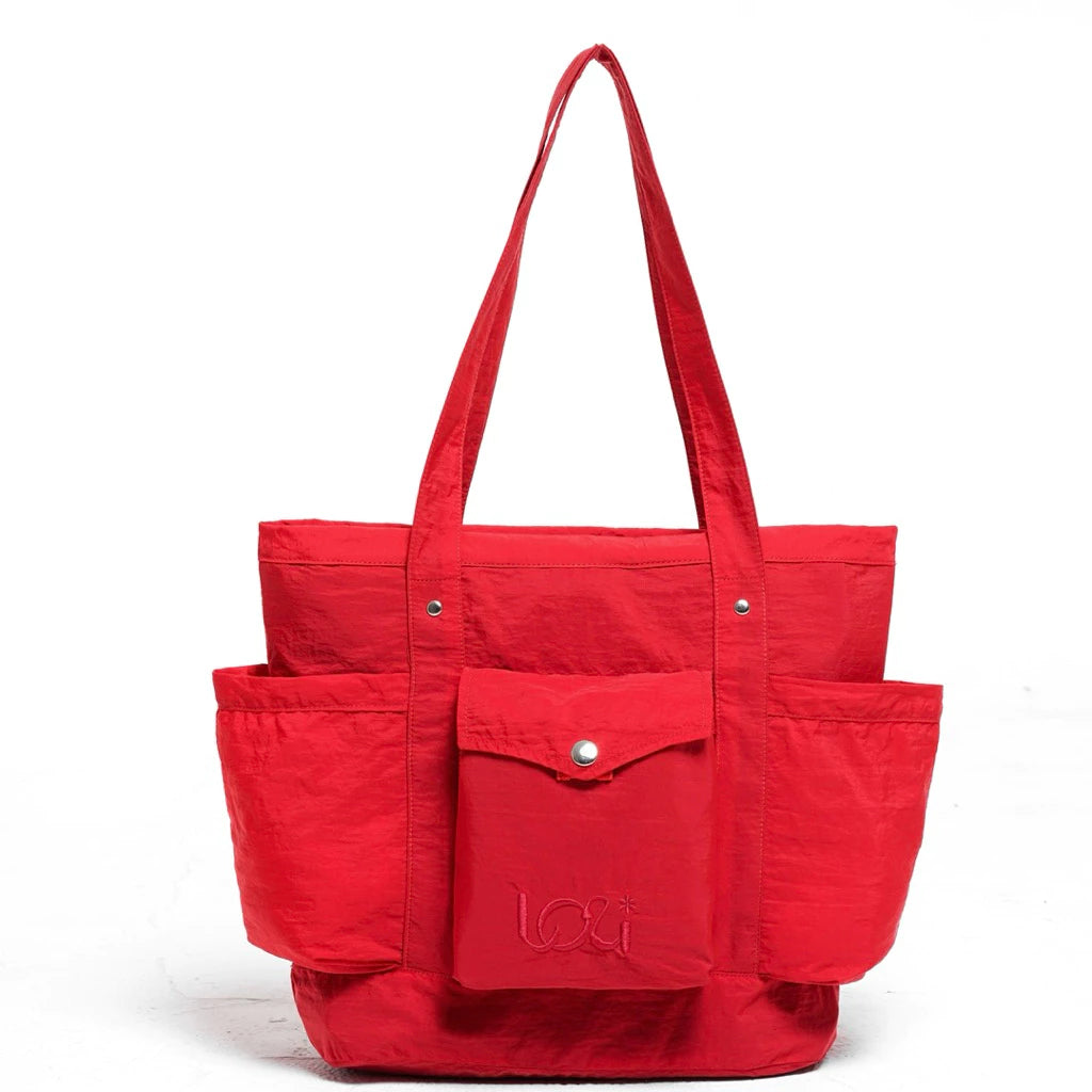 Red women’s tote bag featuring two long handles, a front flap pocket with button closure, and two spacious side pockets.
Tas wanita warna merah dengan desain tote bag, dilengkapi dua handle panjang, satu kantong depan berpenutup kancing, serta dua kantong samping yang luas.