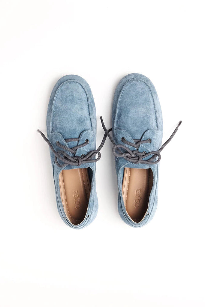 A pair of light blue suede boat flatshoes by Cajsa with dark gray laces, shown from a top-down view on a white background.