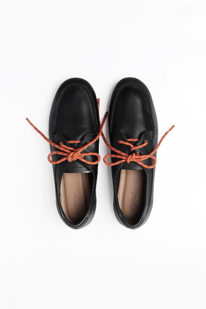 A pair of black leather lace-up flatshoes by Cajsa with contrasting orange-brown laces, shown from a top-down view on a white background.