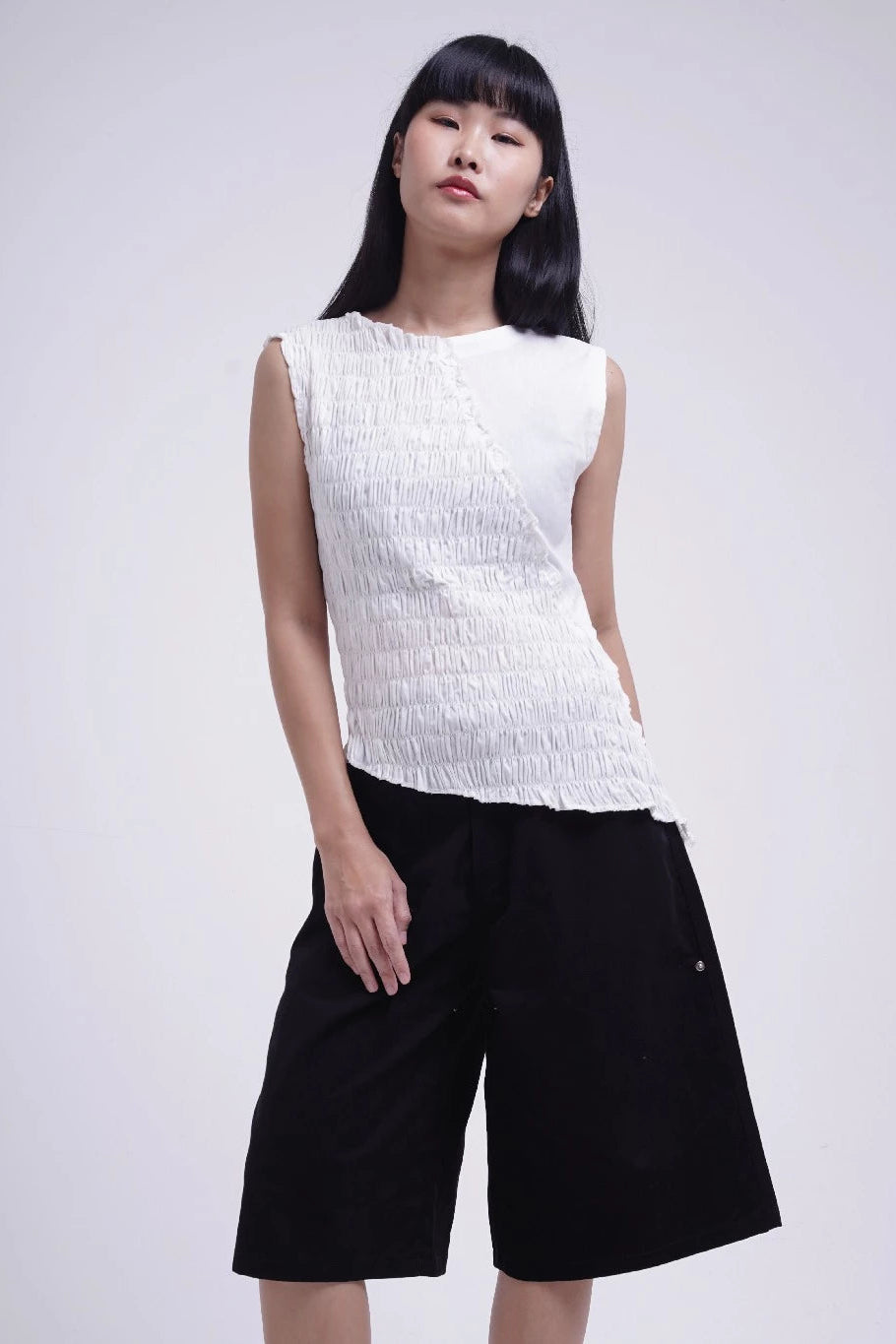 Woman wearing a white sleeveless top and black jorts pants on a plain background