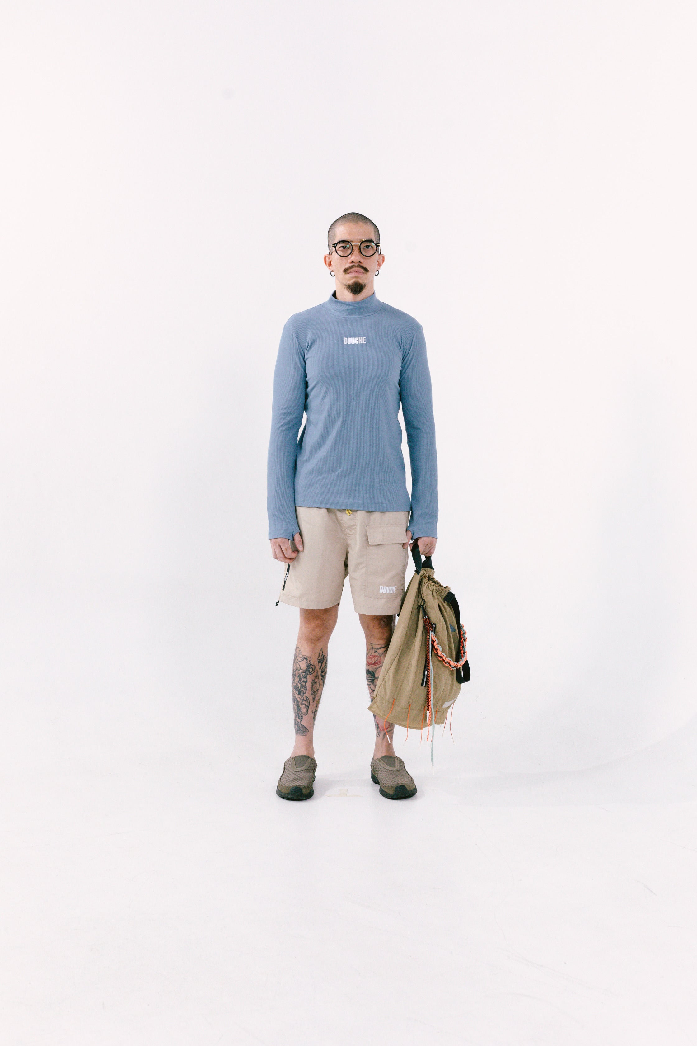Person wearing a blue sweater and beige shorts holding a light brown cuttlefish bag on a white background