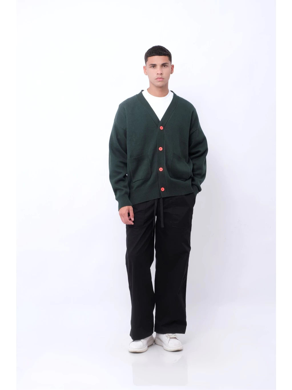 Person wearing a green cardigan with red buttons by Blee, black pants, and white shoes on a white background