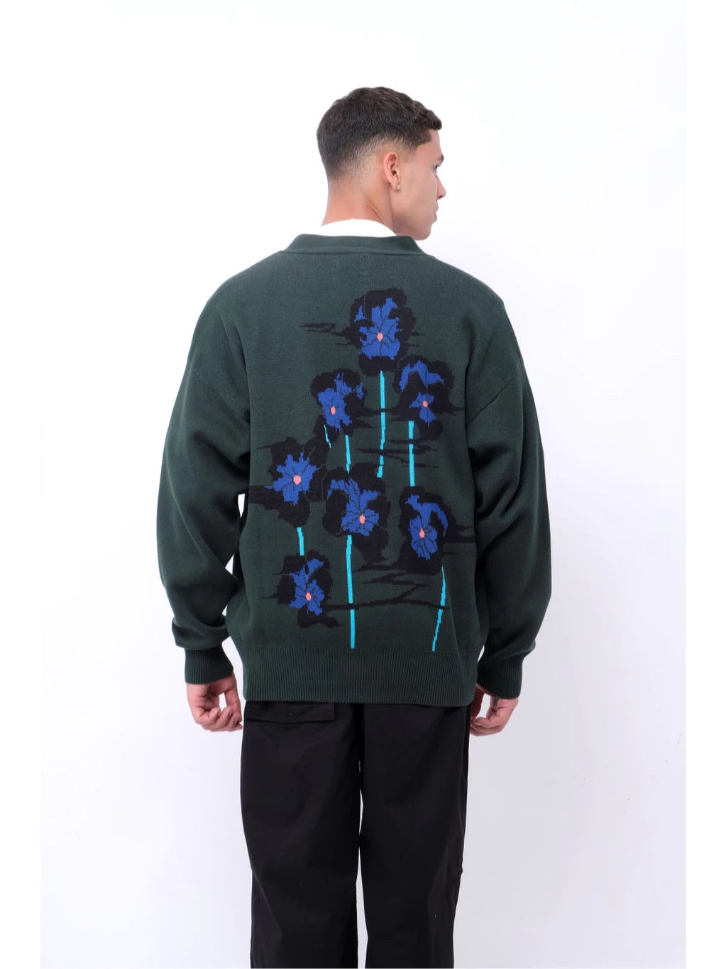 Person wearing a dark green cardigan with blue floral patterns on the back by Blee, standing against a white background.