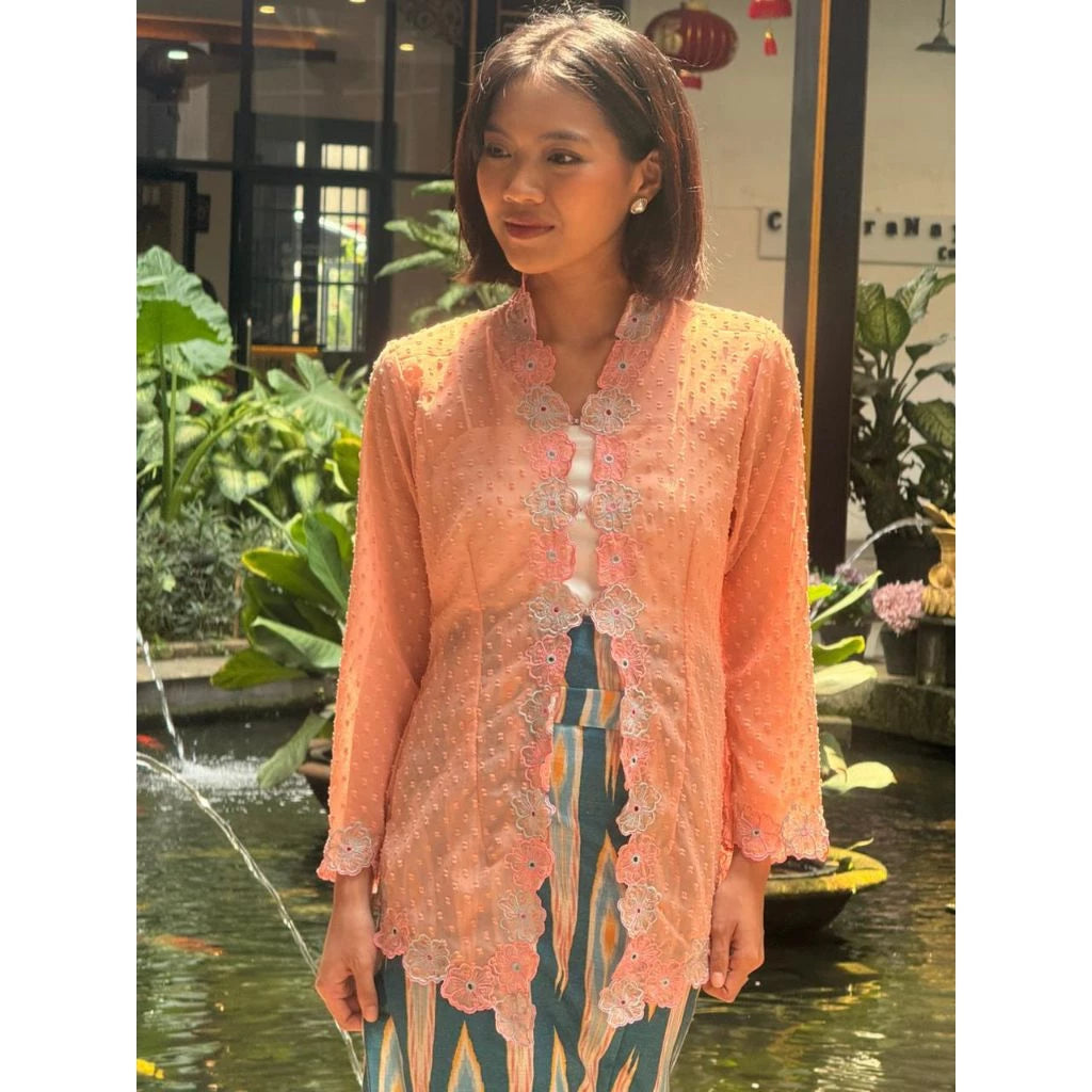 Woman in a peach lace tunic by Merona standing by a fountain with greenery in the background.
Seorang wanita mengenakan tunik renda berwarna peach dari Merona berdiri di samping air mancur dengan latar belakang pepohonan hijau.