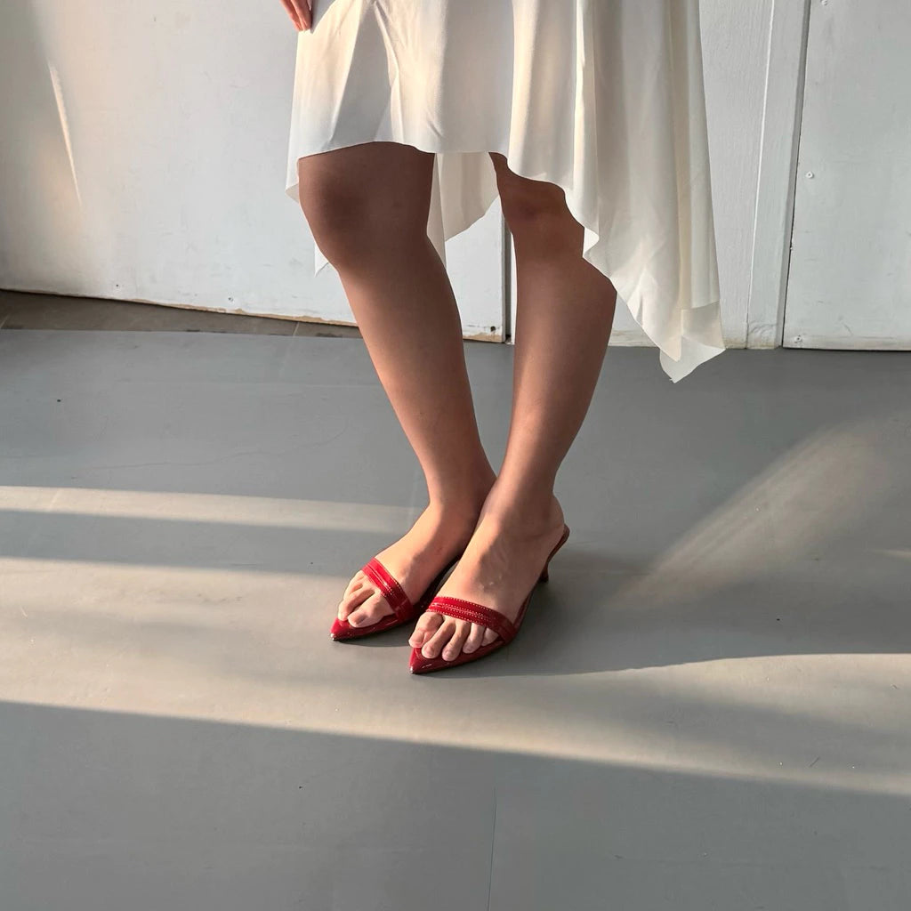Person wearing red sandals by Takkan and a white dress standing on a gray floor with sunlight casting shadows.