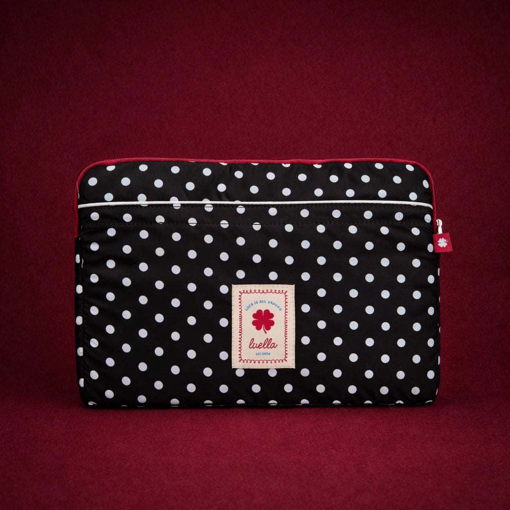 Black polka dot laptop sleeve by Luella with a brand label on a red background