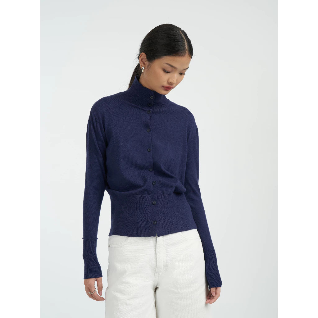 Woman wearing a navy blue turtleneck cardigan by Achete de Nous with a white background