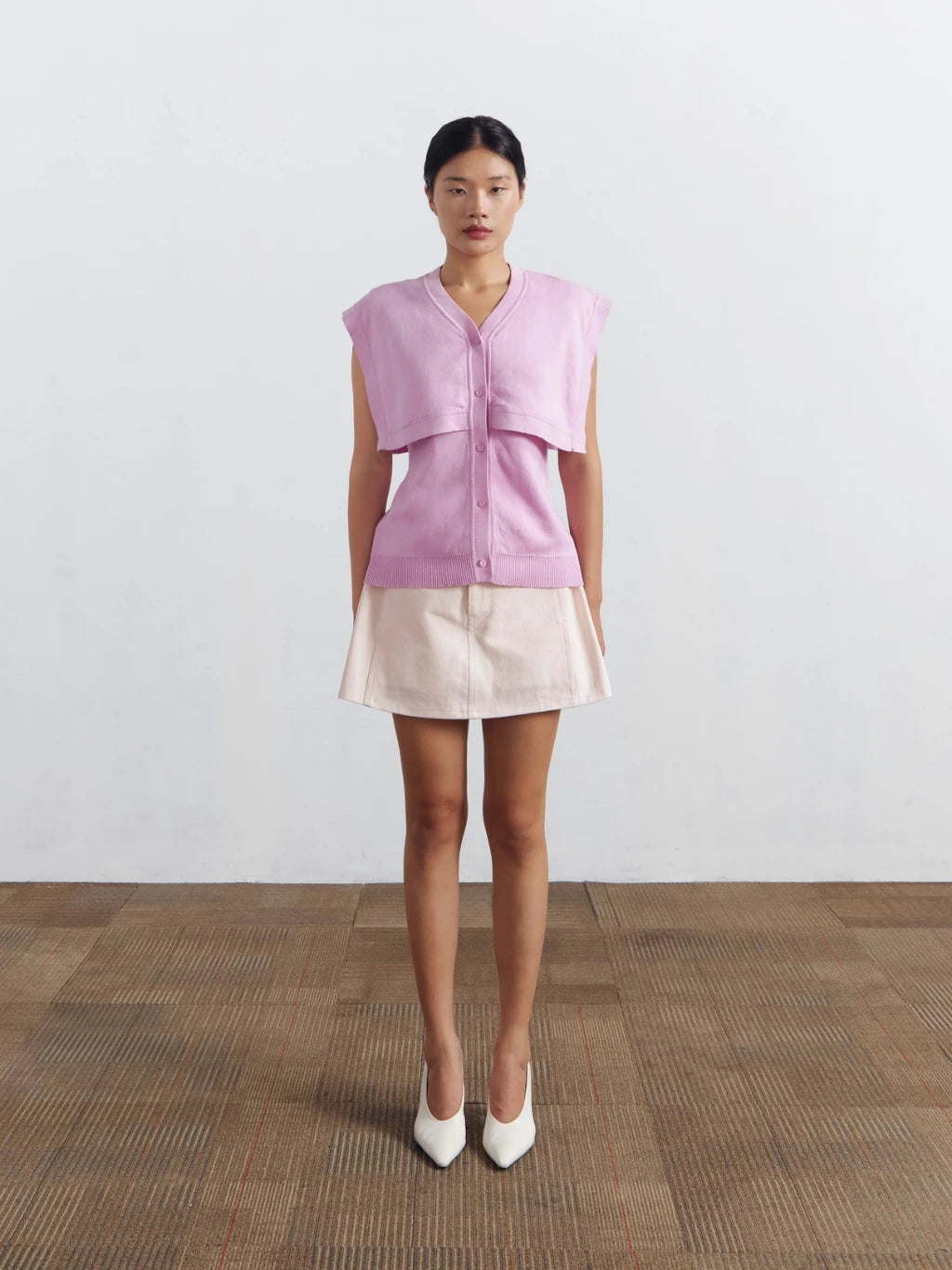 Woman wearing a pink sleeveless vest by Achete de Nous and beige skirt on a plain background