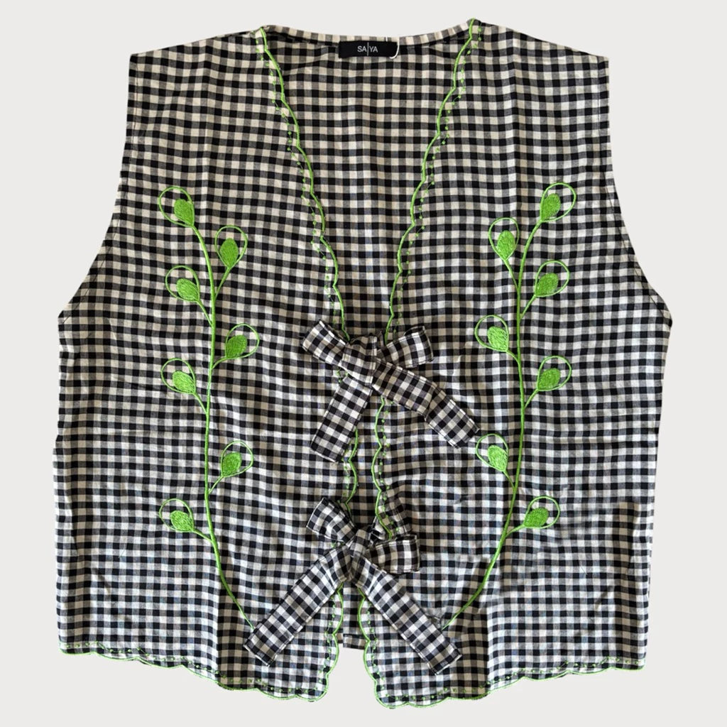 Black and white checkered vest with green floral embroidery on a light gray background
