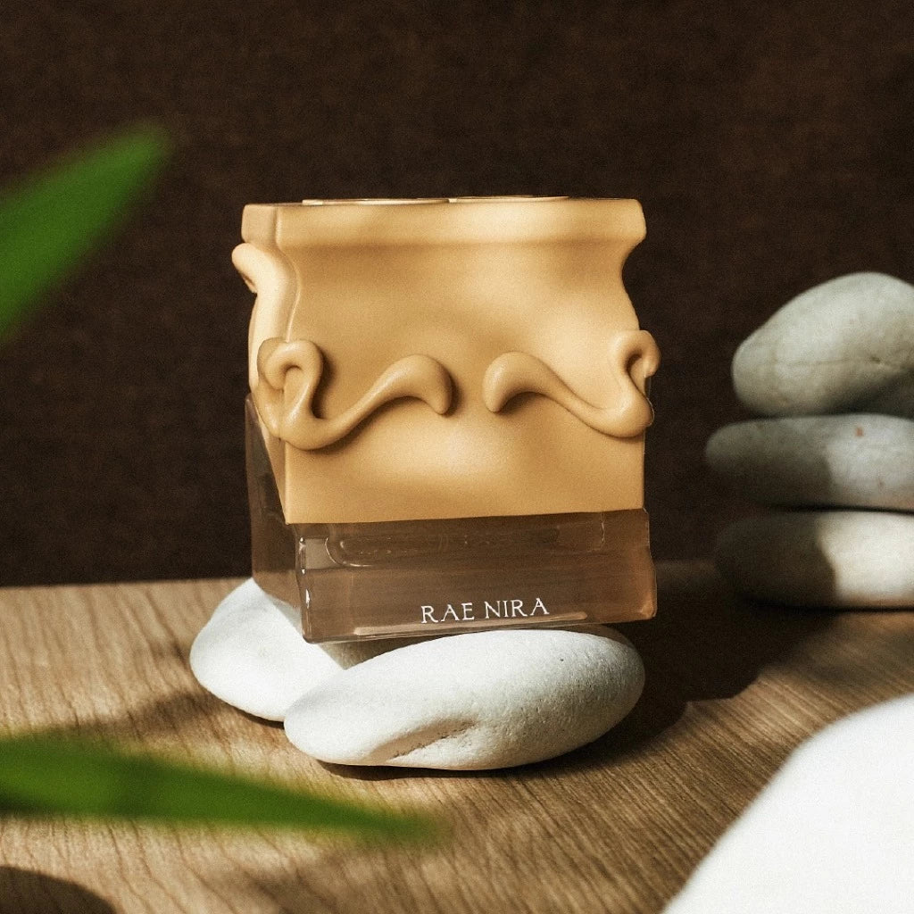 Rae Nira perfume bottle by Saff & Co. with decorative design on cap, placed on stones with a blurred background