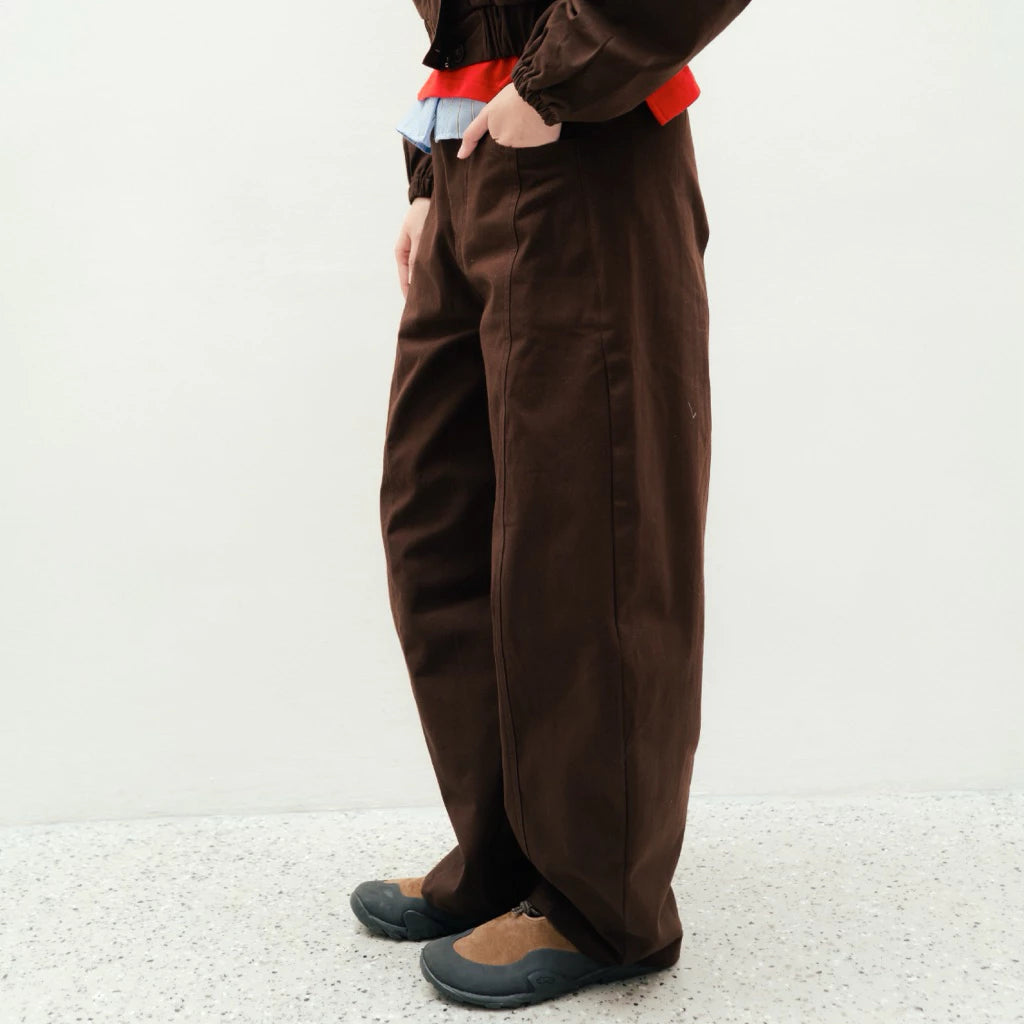Person wearing brown wide-leg pants by notyourcompany and a red top on a white background