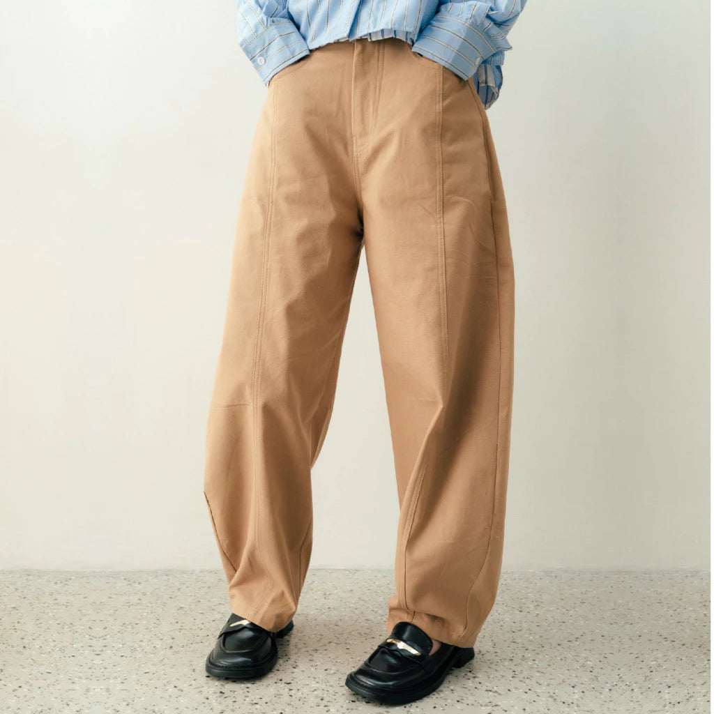 Person wearing cream wide-leg pants by notyourcompany and a blue plaid shirt against a plain background