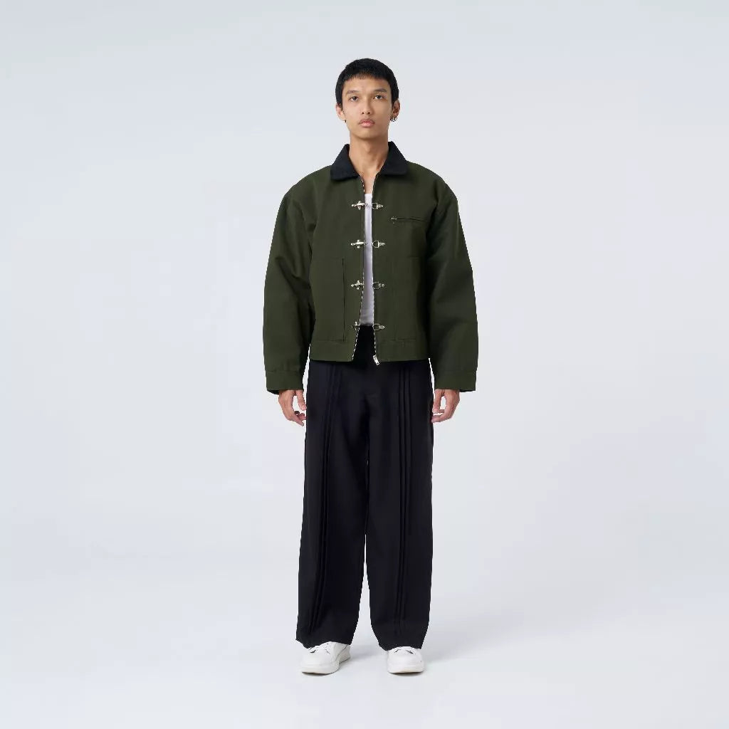 Person wearing a green fireman clasp jacket by Blee and black pants on a white background