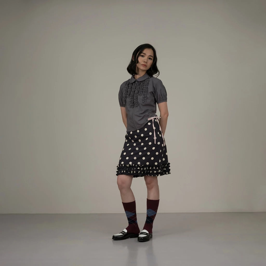 Woman wearing a gray top and black polka dot skirt against a plain background
