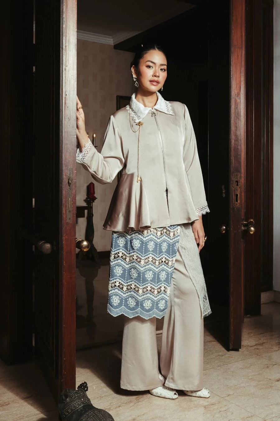 Woman in a beige top by LR Studio and pants with a patterned skirt standing in a doorway.