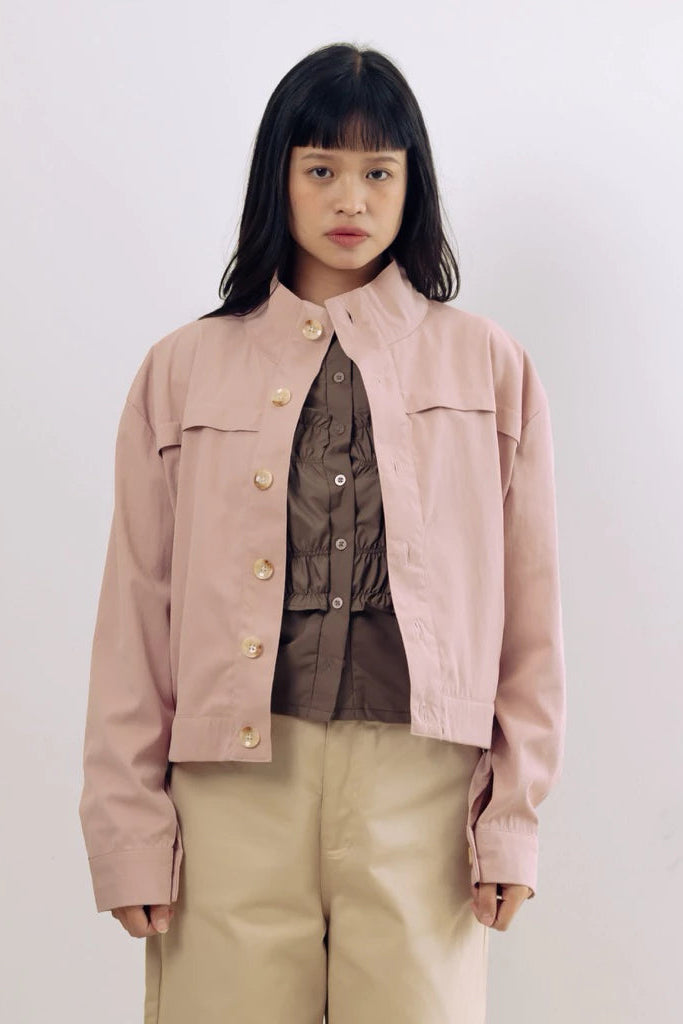 Person wearing a light pink jacket by notyourcompany over a brown shirt with beige pants on a white background