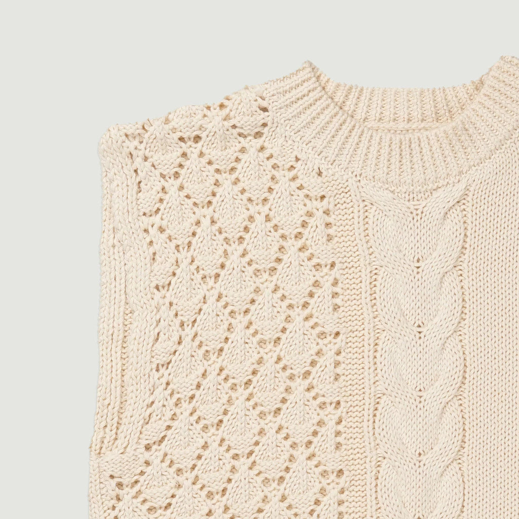 Close-up of a beige knitted vest with cable pattern on a light gray background