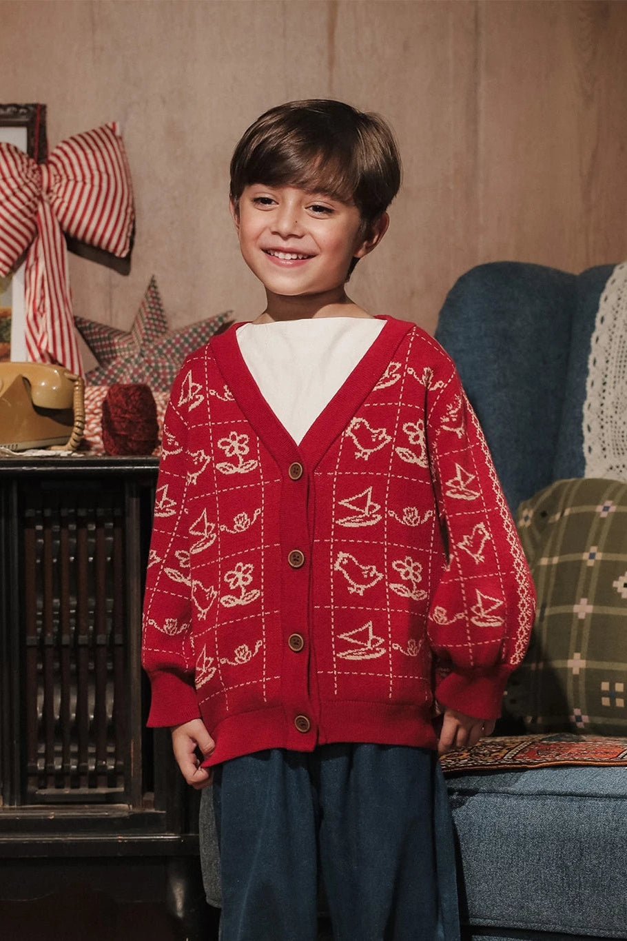 Child wearing a red cardigan with white patterns by Sabine & Heem kids clothing in a cozy living room setting