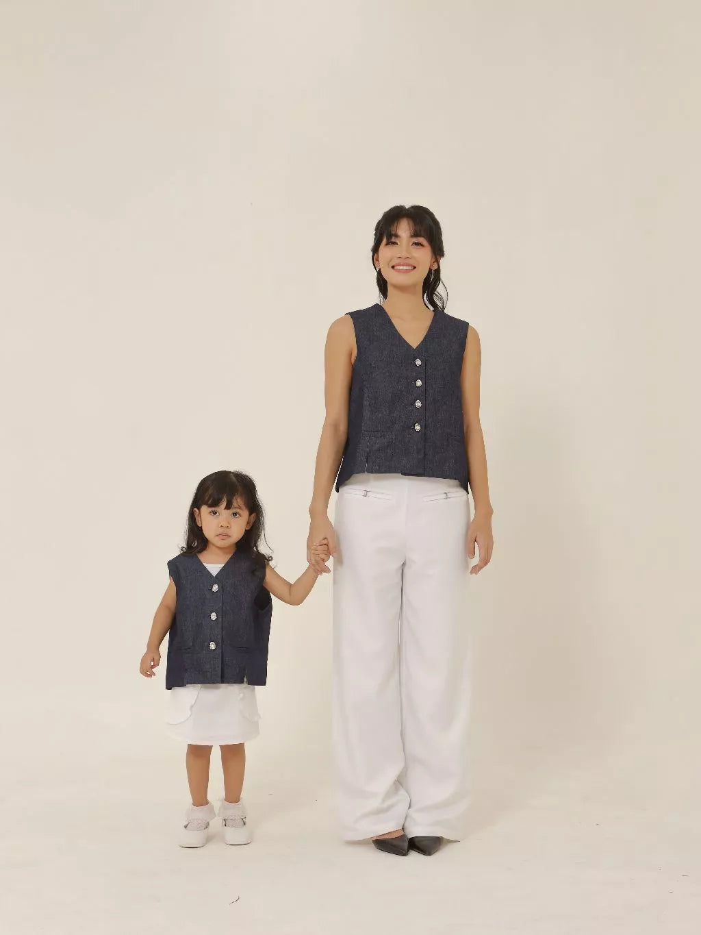 Woman and child wearing matching navy vests and white pants on a plain background