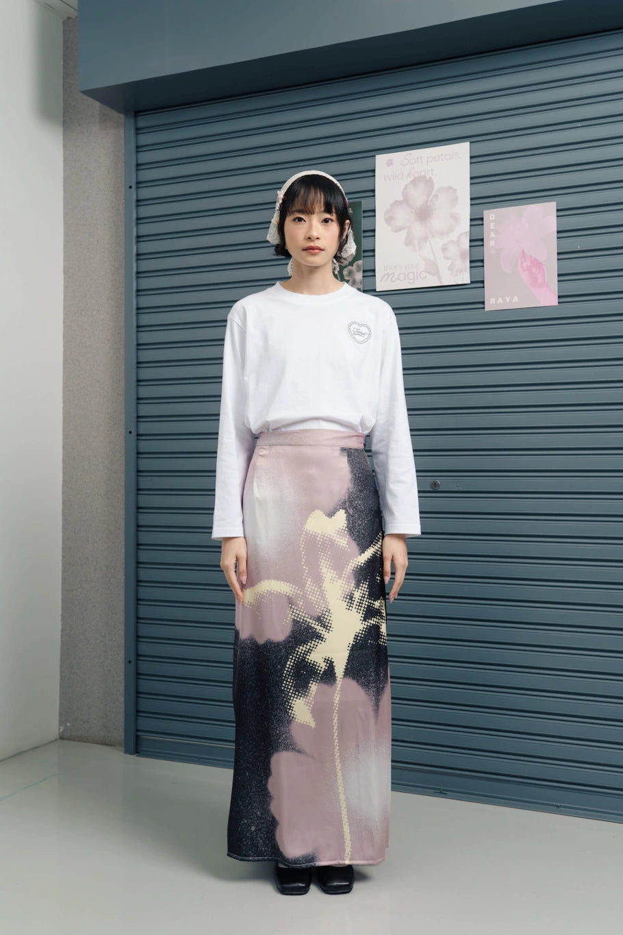 Person wearing a white top and a long, patterned skirt by Tome Ame standing in front of a blue shutter.