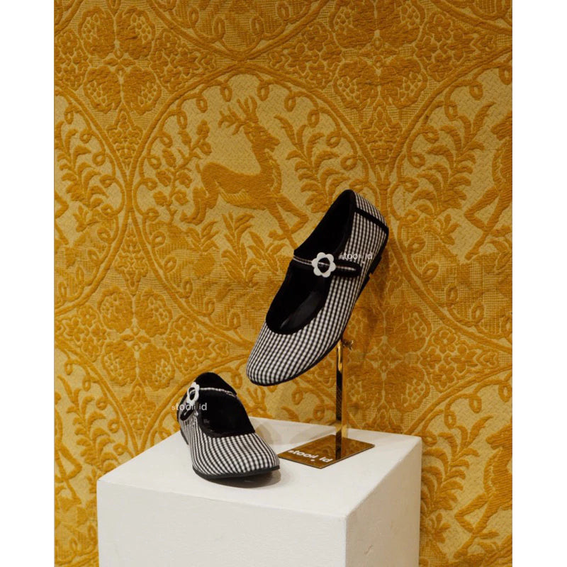 Black and white checkered flatshoes on a stand against a decorative yellow wall.