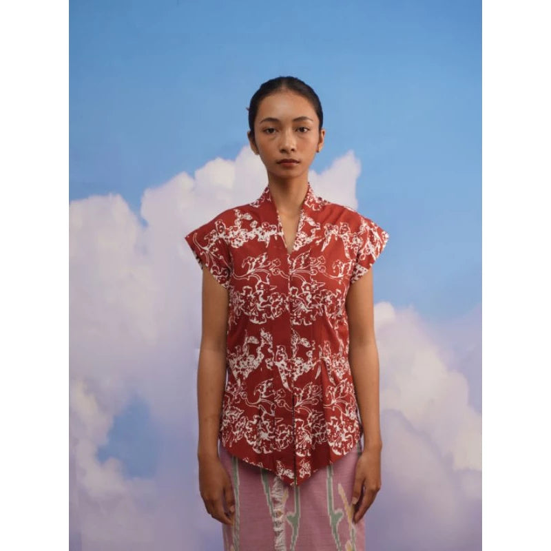 Person wearing a red and white floral patterned kebaya by Manikan with a blue sky and clouds in the background